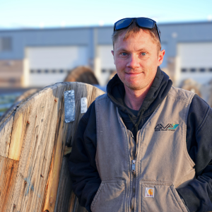 Photo of Tyler leaning against a wooden spool.